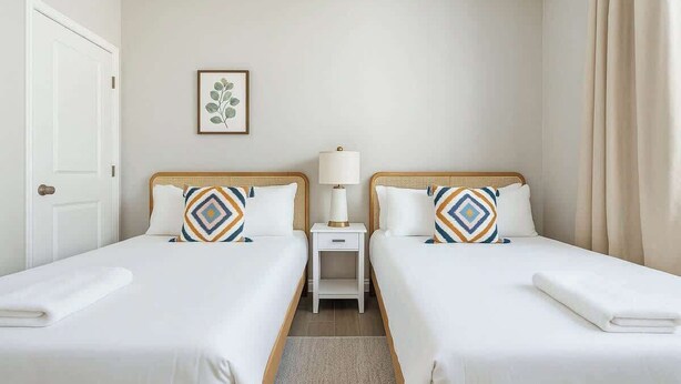 Une chambre d’hôtel avec deux lits simples, une petite table de chevet avec une lampe et un tableau encadré au mur.