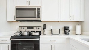 Une cuisine moderne avec des meubles blancs, un four à micro-ondes encastré, une cuisinière avec des casseroles, une machine à café et un grille-pain.