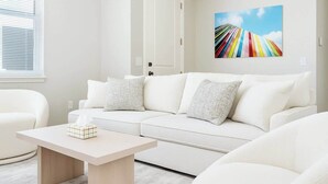 Un salon moderne avec un canapé blanc, une petite table et un tableau abstrait aux couleurs vives accroché au mur.