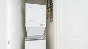 Une petite buanderie blanche, équipée d’un lave-linge et d’un sèche-linge à chargement frontal, d’un panneau de commande et de tuyauterie visible.