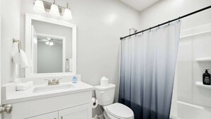 Une salle de bain avec un meuble-lavabo blanc, un miroir, des toilettes et un rideau de douche.