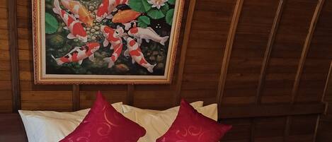 A hotel room with a wooden ceiling, a bed with white bedding and red pillows, and a framed painting of koi fish above the bed.