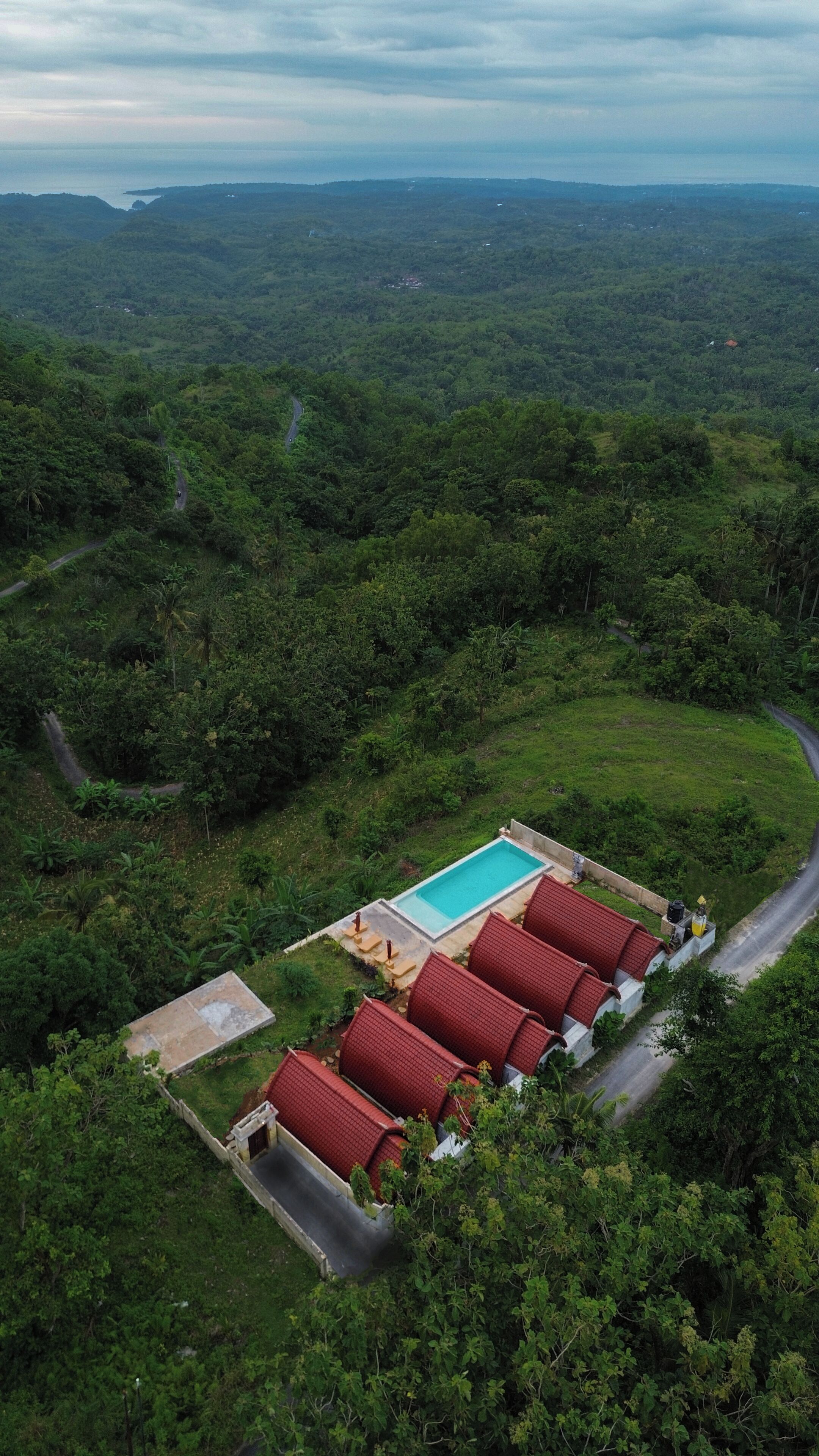 An aerial view of a resort with a swimming pool, red-roofed buildings, and a winding road.