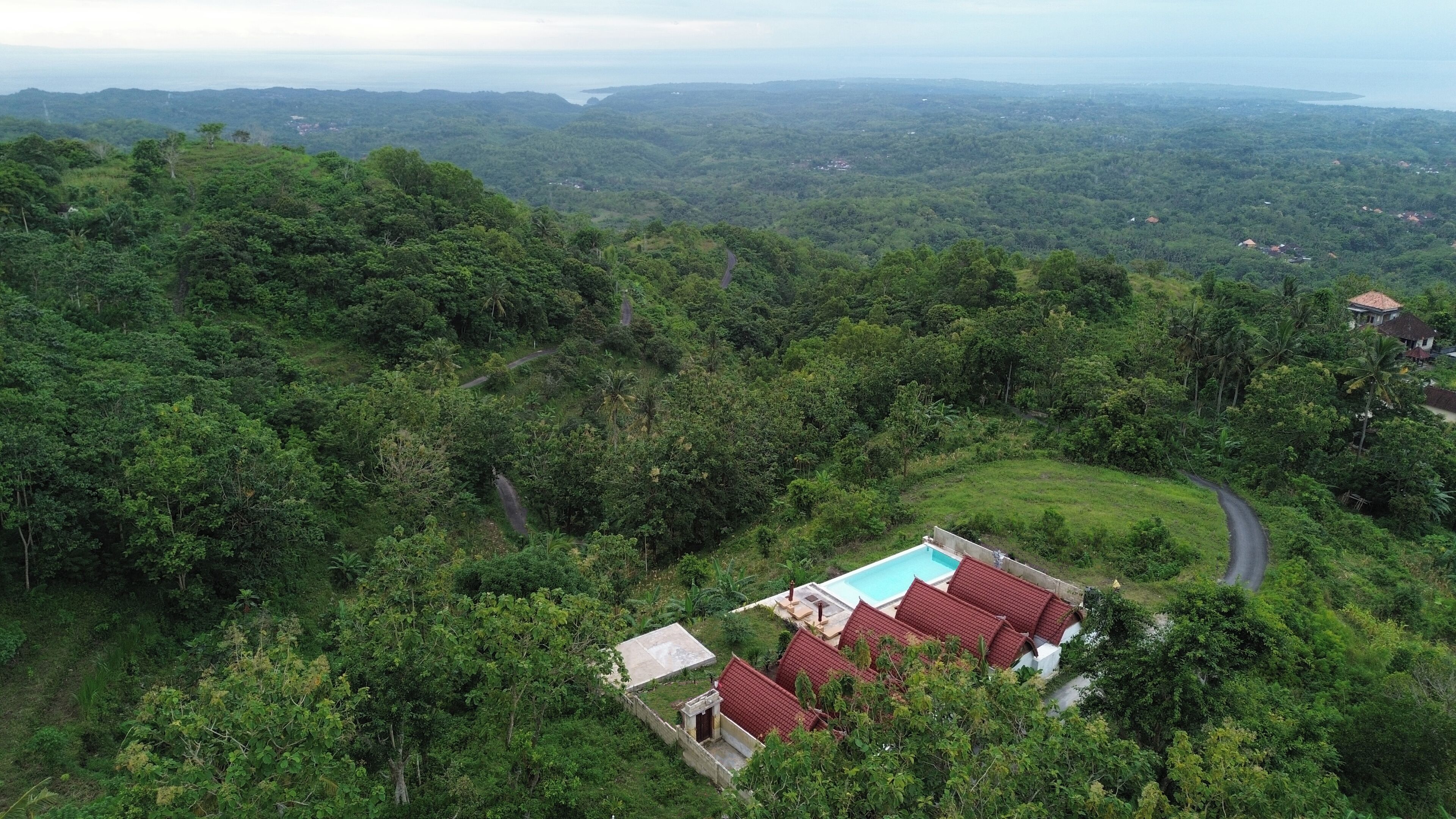 A secluded villa with a swimming pool, surrounded by dense forest and a winding road.