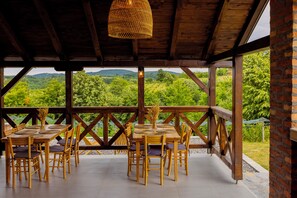 Een houten terras buiten, met een tafel voor zes personen, omringd door stoelen, met uitzicht op een weelderig groen landschap.