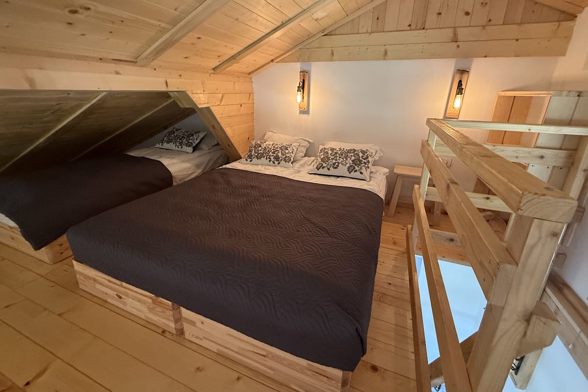 Una cabaña de madera con un dormitorio en el altillo, una cama litera y una pequeña escalera de madera.