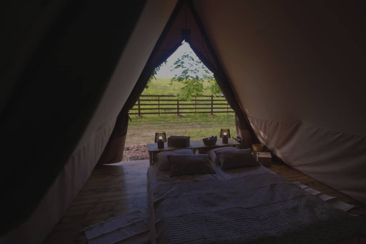 Une tente avec un lit Ă lâintĂ©rieur, une vue sur une zone herbeuse Ă lâextĂ©rieur et une clĂŽture au loin.