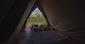 A tent with a bed inside, a view of a grassy area outside, and a fence in the distance. - My little Farm Agroturizam (Ogladjenovac)
