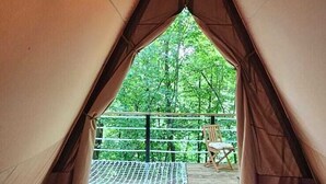 Una carpa con dos camas, vistas al verdor exterior y una silla en el balcón.