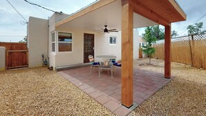 Un espacio de patio cubierto con una mesa, sillas, ventilador de techo y una estructura de pérgola de madera.