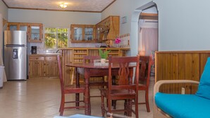 A cozy kitchen with wooden cabinets, a dining table with chairs, a sofa, and a refrigerator. - Roatan Ocean View - Ground Floor 2 Bedroom Apts (Roatan)