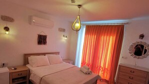 A bedroom with a wooden floor, a bed with a headboard, a nightstand, a dresser, and a window with orange curtains. - Paris Alacati Butik Otel (Cesme)