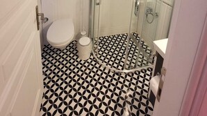 Un baño con inodoro, ducha con puerta de vidrio y suelo estampado.