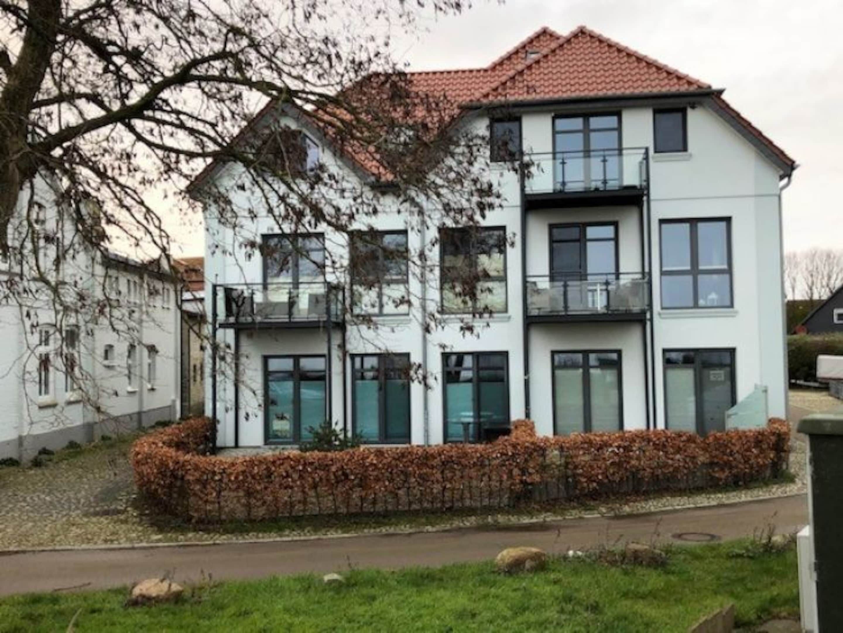 A multi-story residential building with a tiled roof, large windows, and a landscaped garden area.