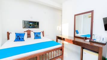 Habitación de hotel con cama, escritorio de madera, espejo, televisor y refrigerador pequeño.