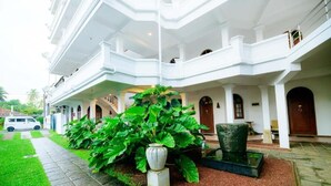 Un edificio de varios pisos con un patio central, plantas verdes grandes y fachada blanca.
