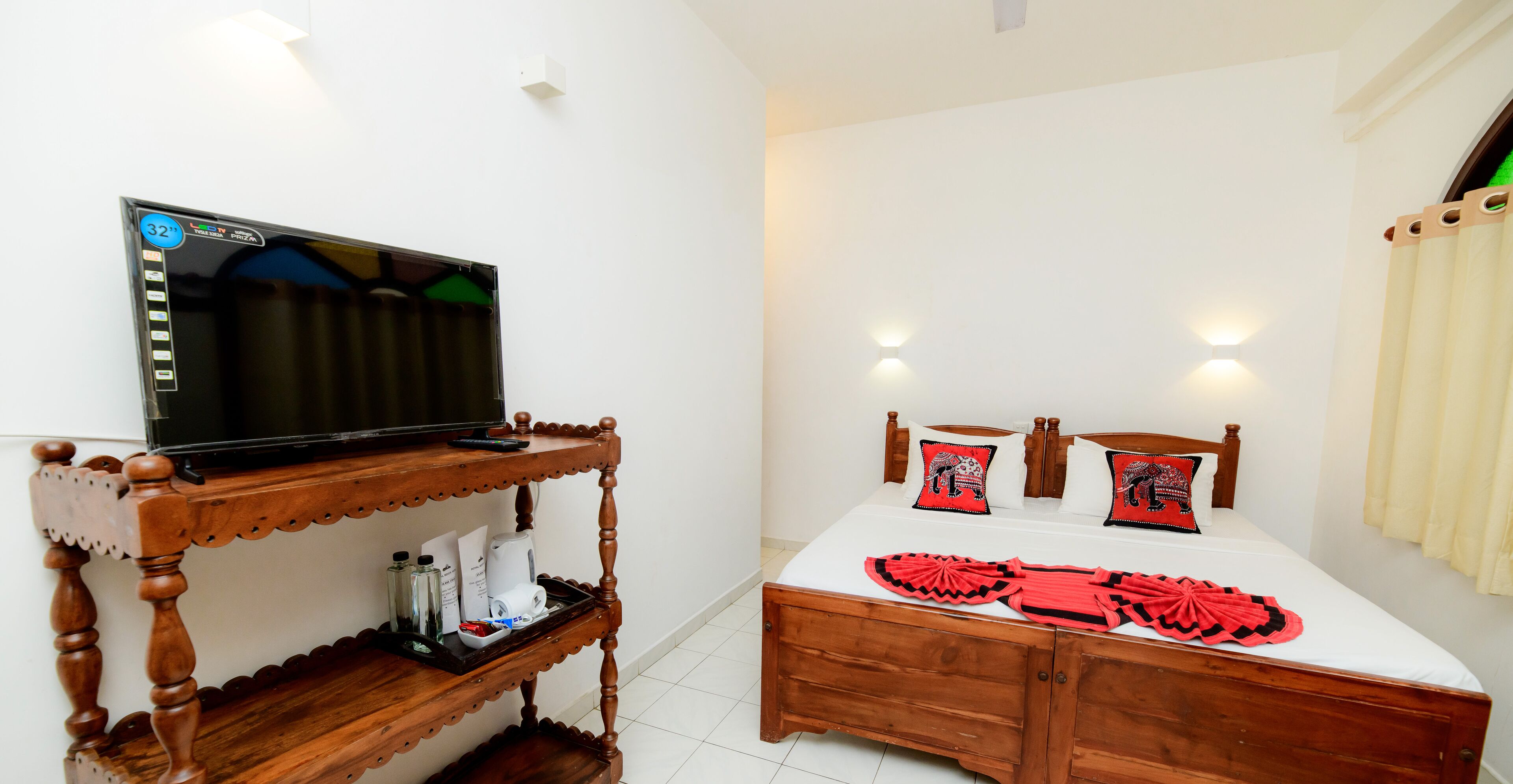 A bedroom with a wooden bed, a TV on a wooden stand, and a white wall with a light fixture.