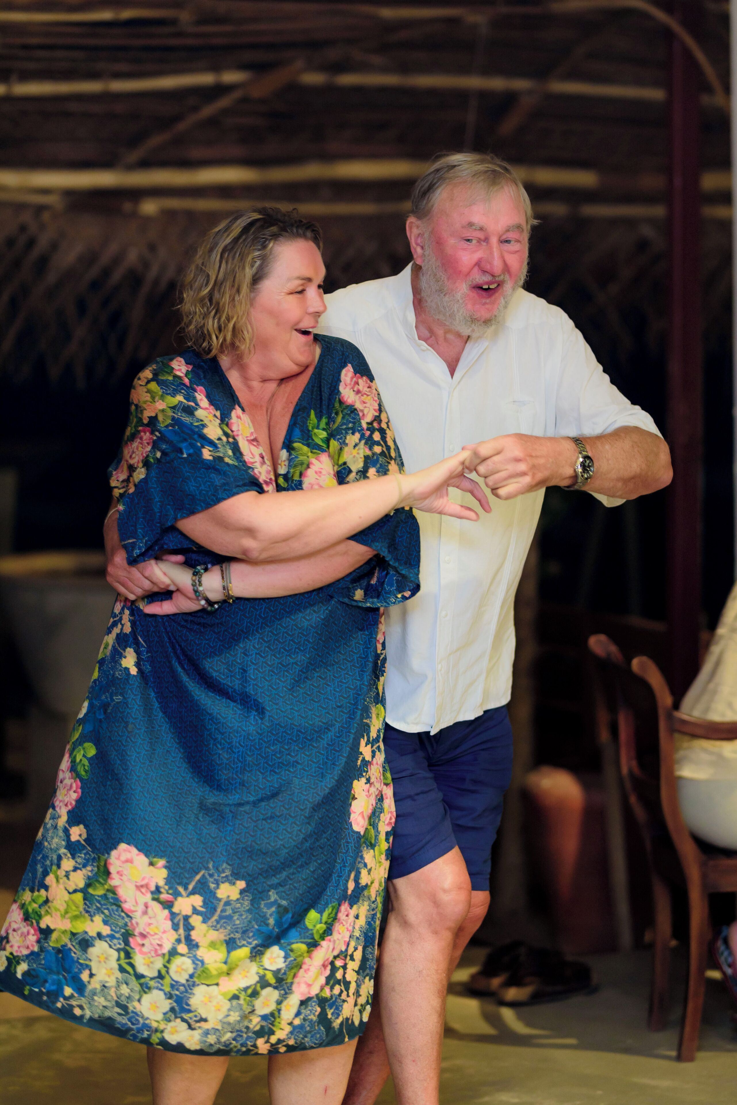 A couple dancing in a room with a thatched roof and wooden furniture.