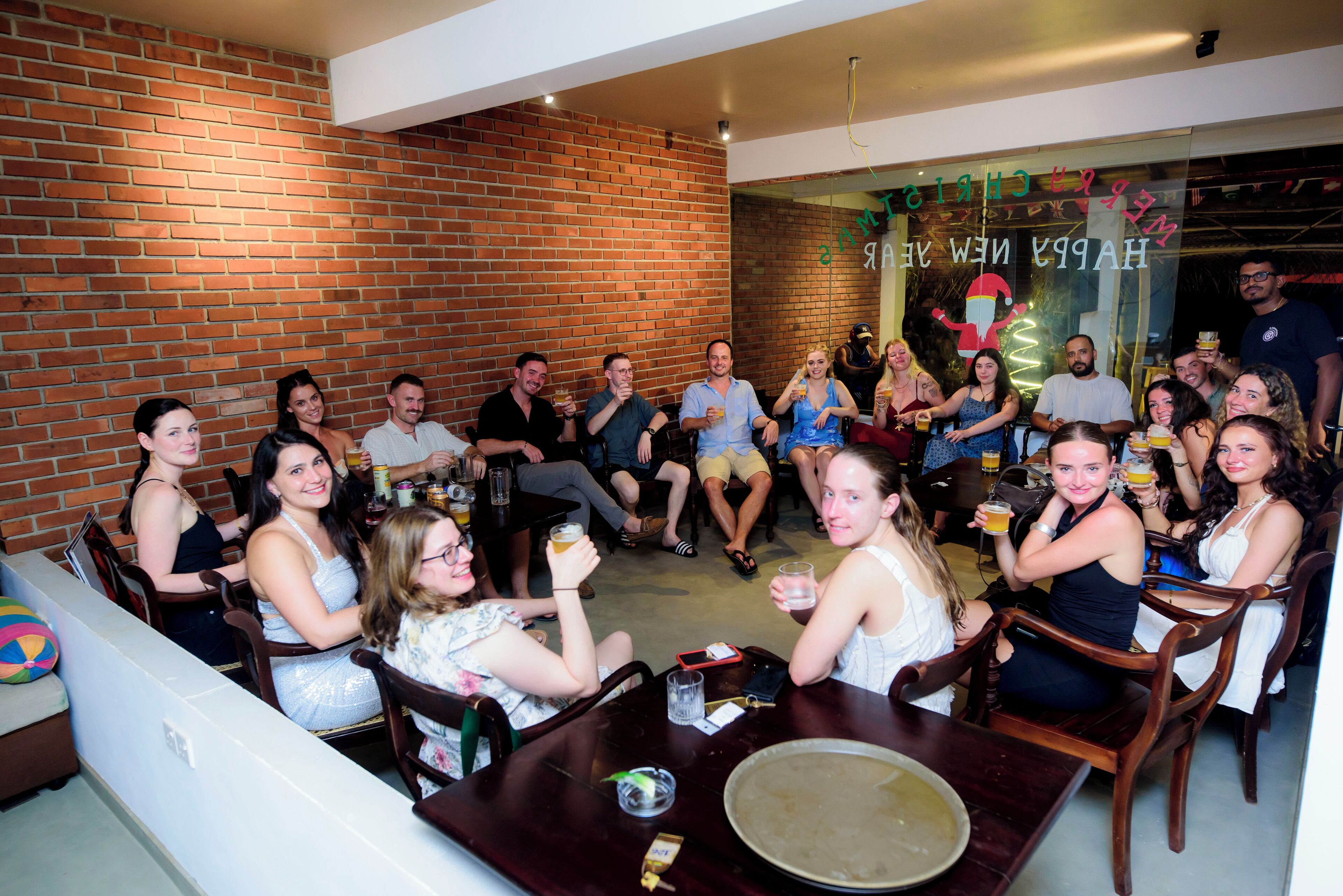 A group of people seated around a table in a room with brick walls and a glass partition displaying "HAPPY NEW YEAR".