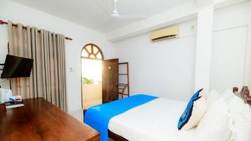 Quarto de hotel com uma cama, uma escrivaninha, televisão, janela com cortinas e ar condicionado.