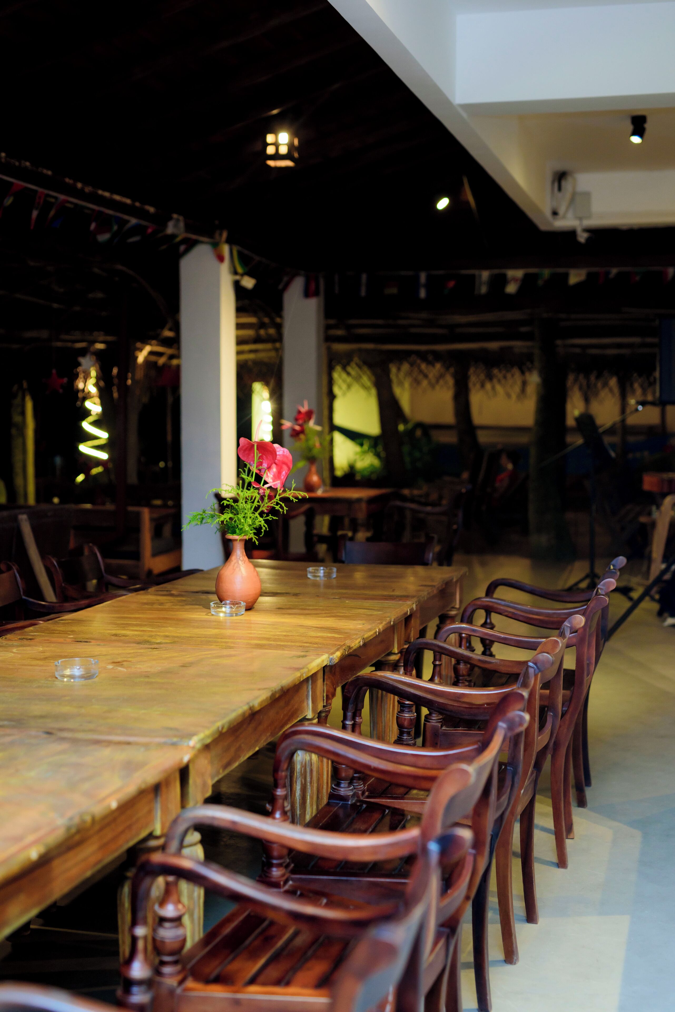 A long wooden dining table with chairs, a vase with flowers, and a modern ceiling with recessed lighting.