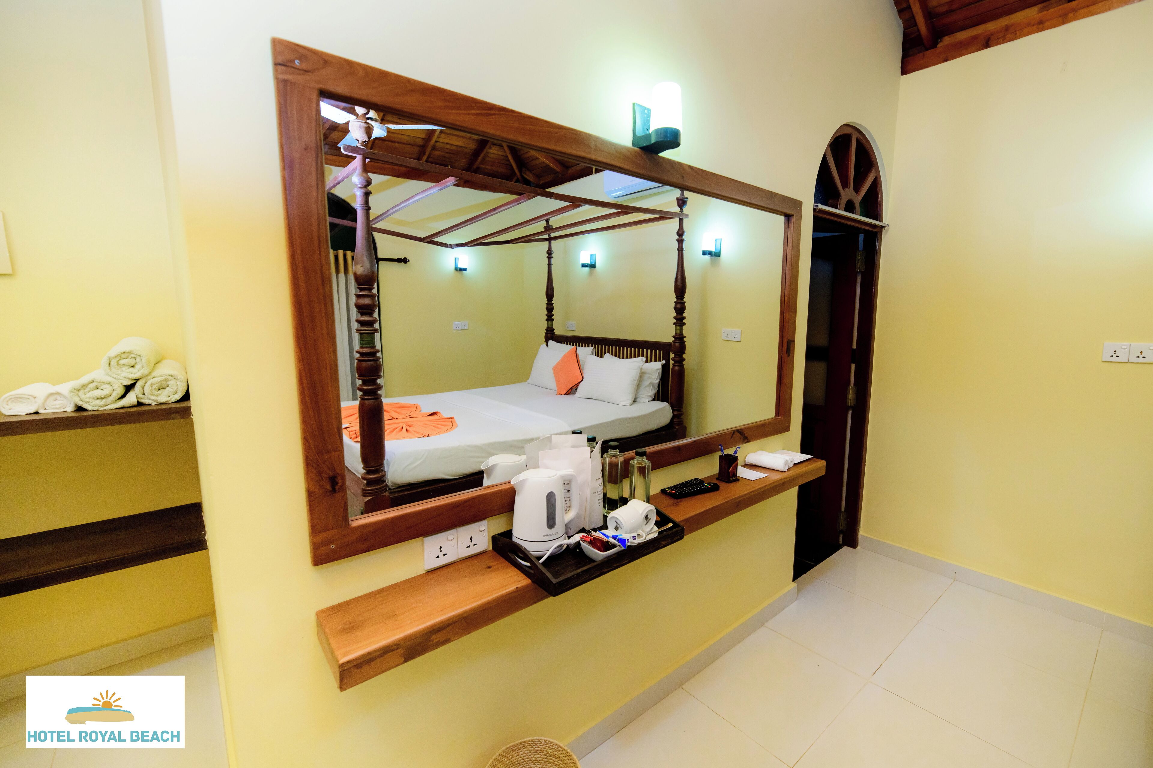 Habitación de hotel con cama con dosel, mesita de noche con un atril de artículos de aseo y un espejo grande sobre la cama.
