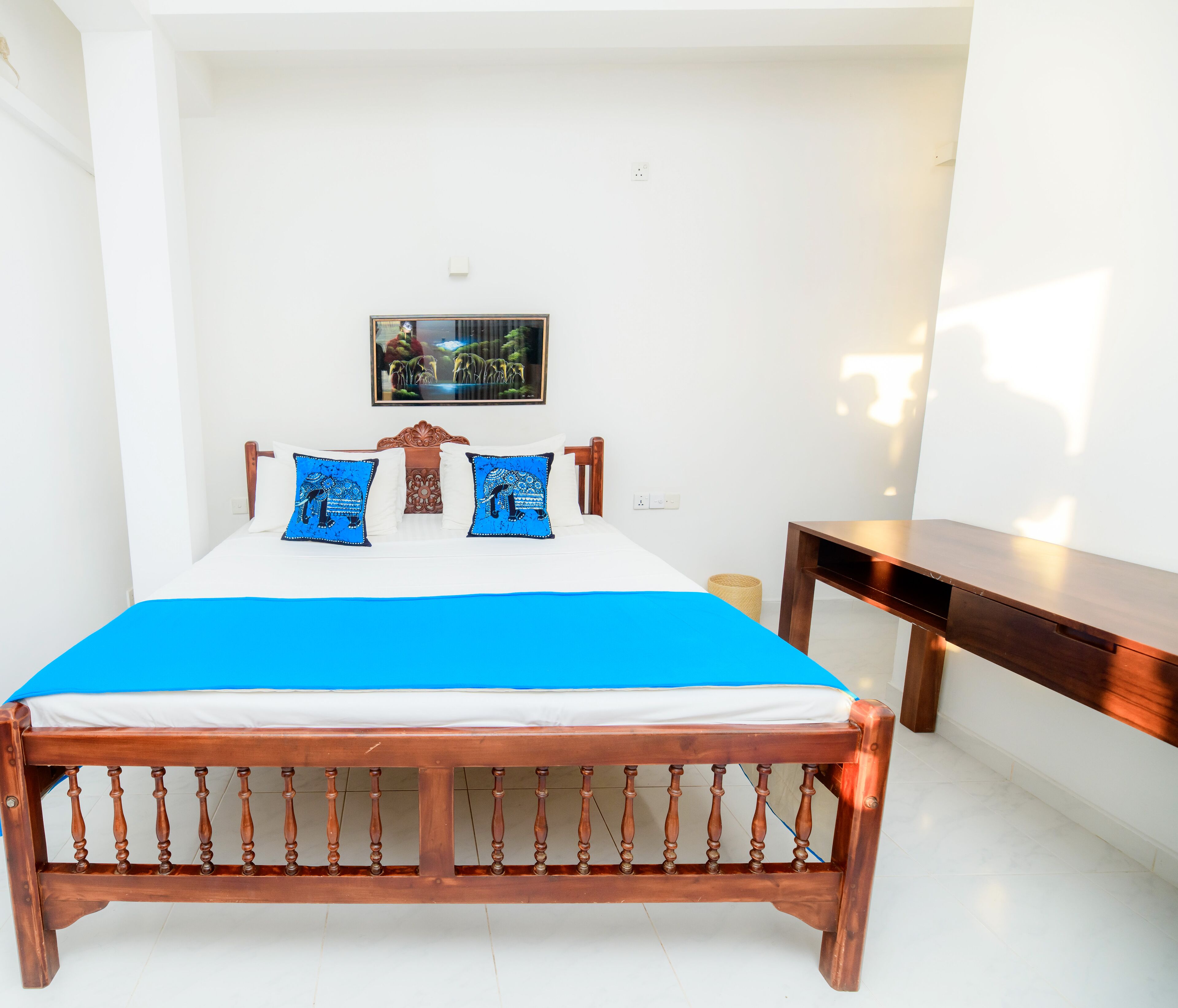 A bedroom with a wooden bed, white walls, a framed picture, and a small wooden table.