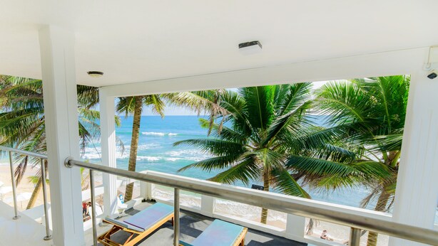Un balcón con vista a la playa y al océano, con sillones de sol y palmeras.