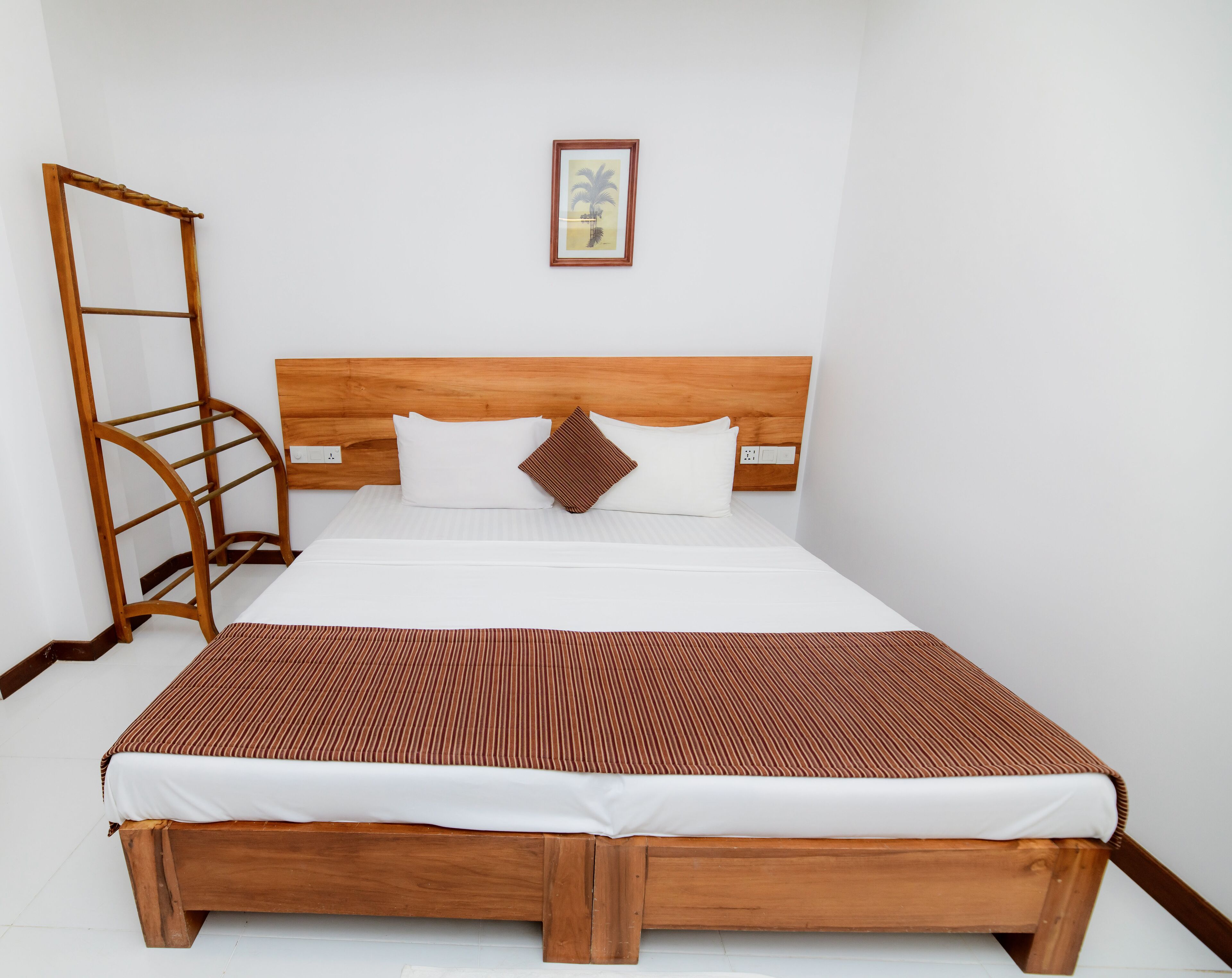 Una cama bien hecha con cabecera de madera, colcha a rayas marrones y una sola almohada marrón.