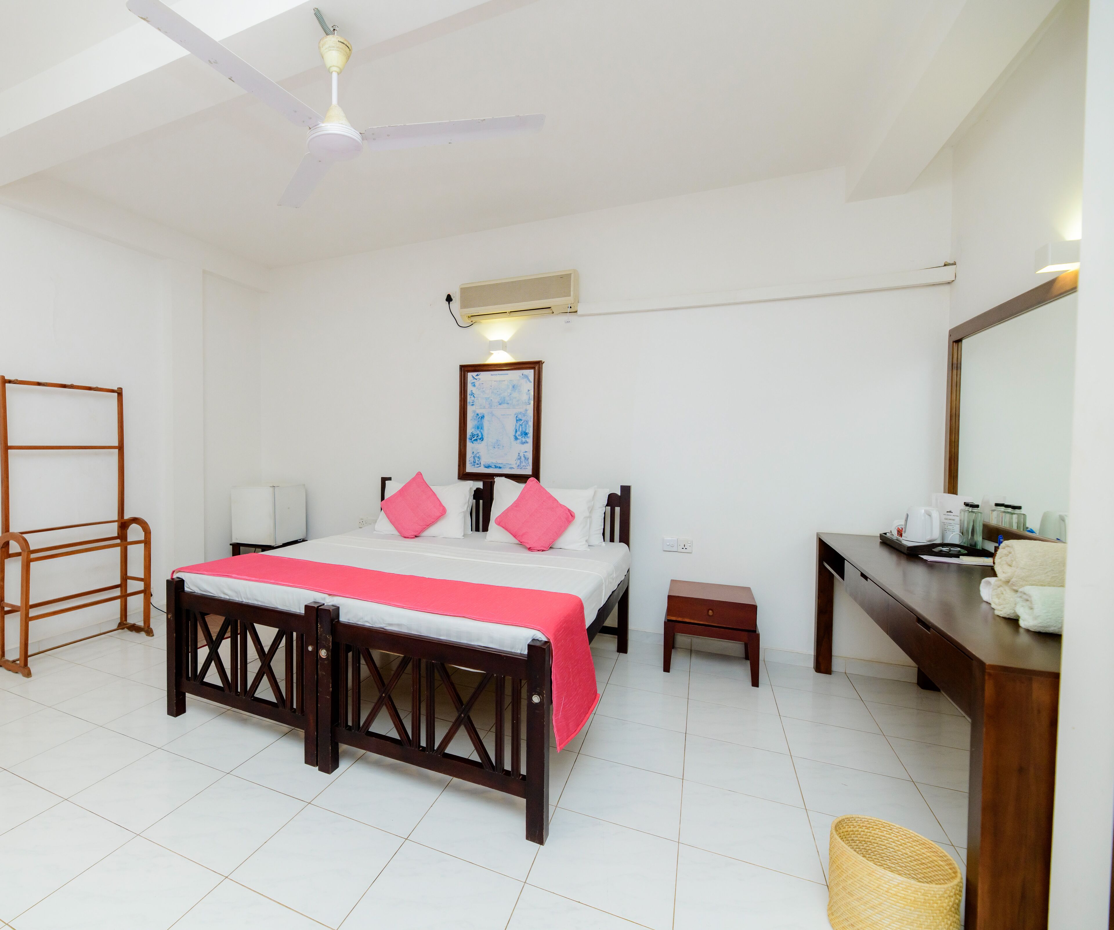 A bedroom with a bed, bedside table, a small stool, a mirror, and a ceiling fan.