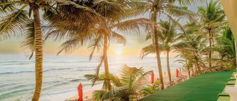 A beach view with palm trees, a sunset, and a beach with lounge chairs and umbrellas.