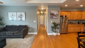 Ein modernes Wohnzimmer mit einer Couch, einem Flur, der zu einer Küche mit Holzschränken und einem Edelstahlkühlschrank führt.