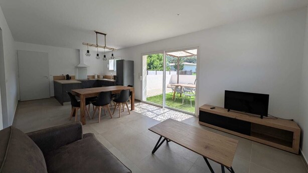 Ein modernes Wohnzimmer mit einer Couch, einem Couchtisch, einer TV-Konsole und einem Essbereich mit Tisch und Stühlen.