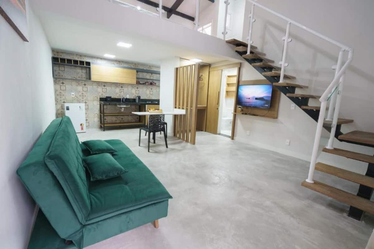 A modern apartment with a green sofa, a kitchen with a built-in oven, a dining area, and a staircase.