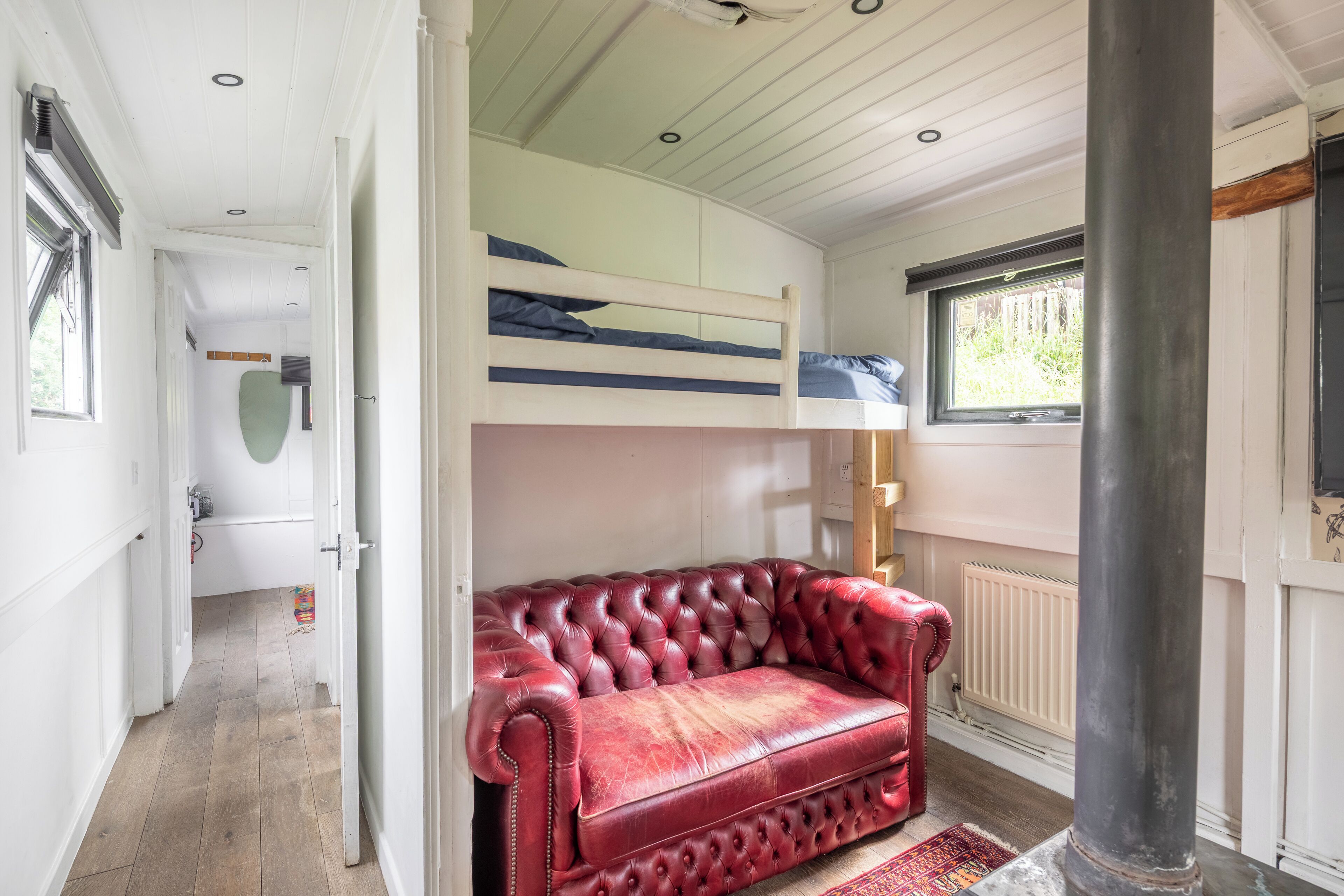 Una habitación con sofá de cuero rojo, literas, un radiador y una ventana.