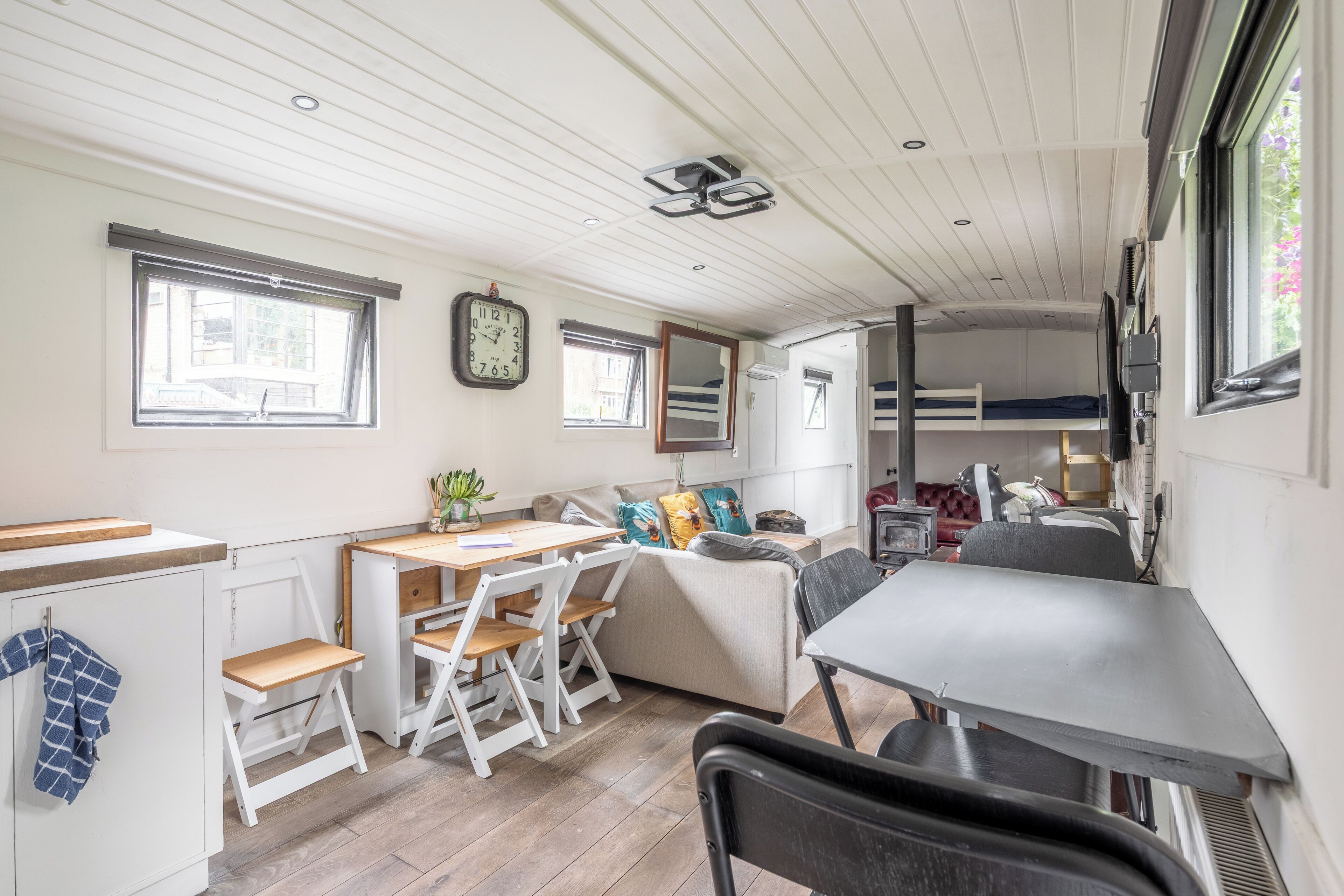 A compact, well-lit room with a kitchenette, a dining area, a sofa, and a bunk bed.