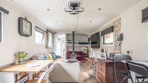 Un interior acogedor con una mesa de comedor de madera, un sofá, un sillón rojo y una zona de cocina con estufa y ventana.
