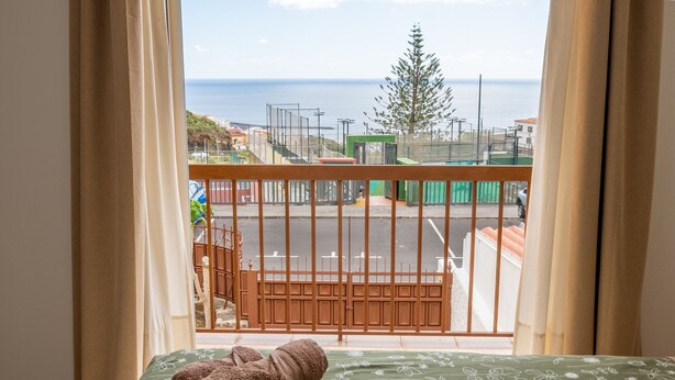 Uma varanda com cama, vista para o mar e cerca verde.