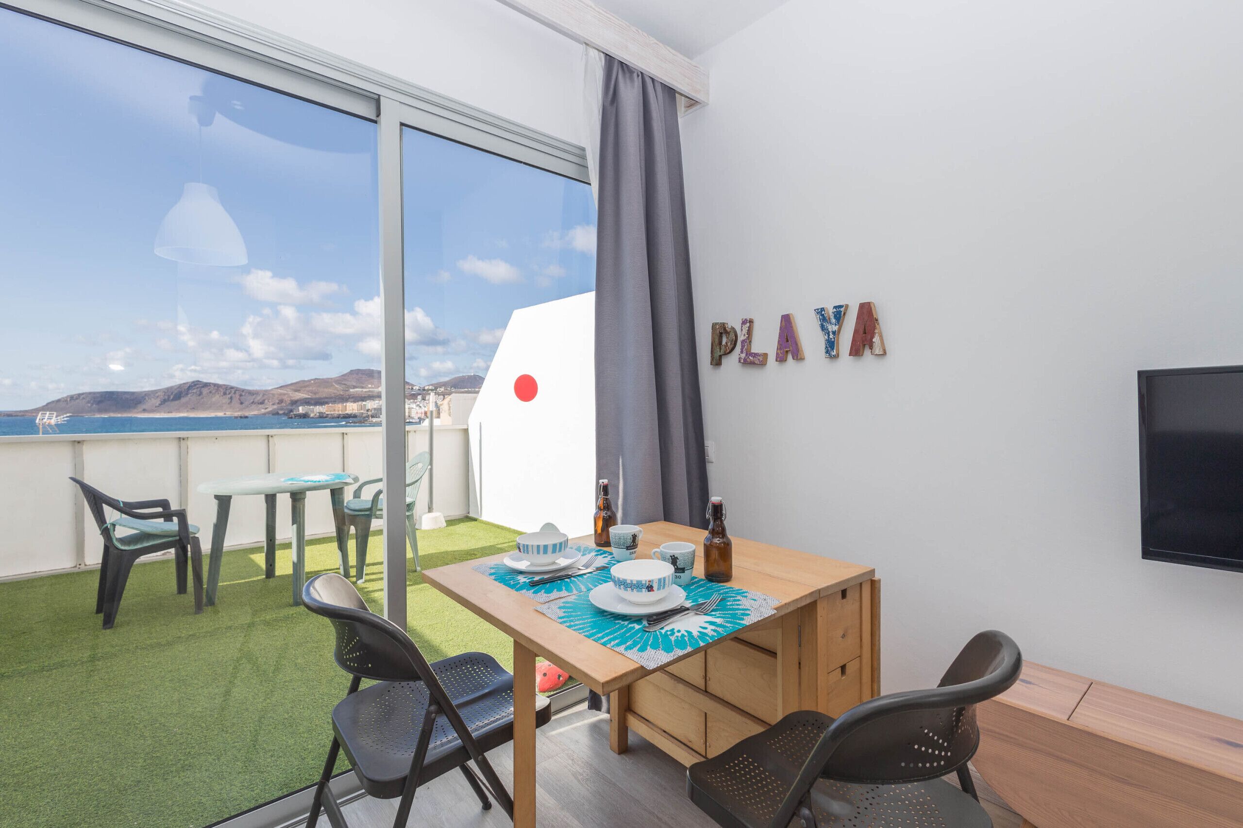 Un balcón con una mesa lista para comer, sillas y un televisor en la pared.