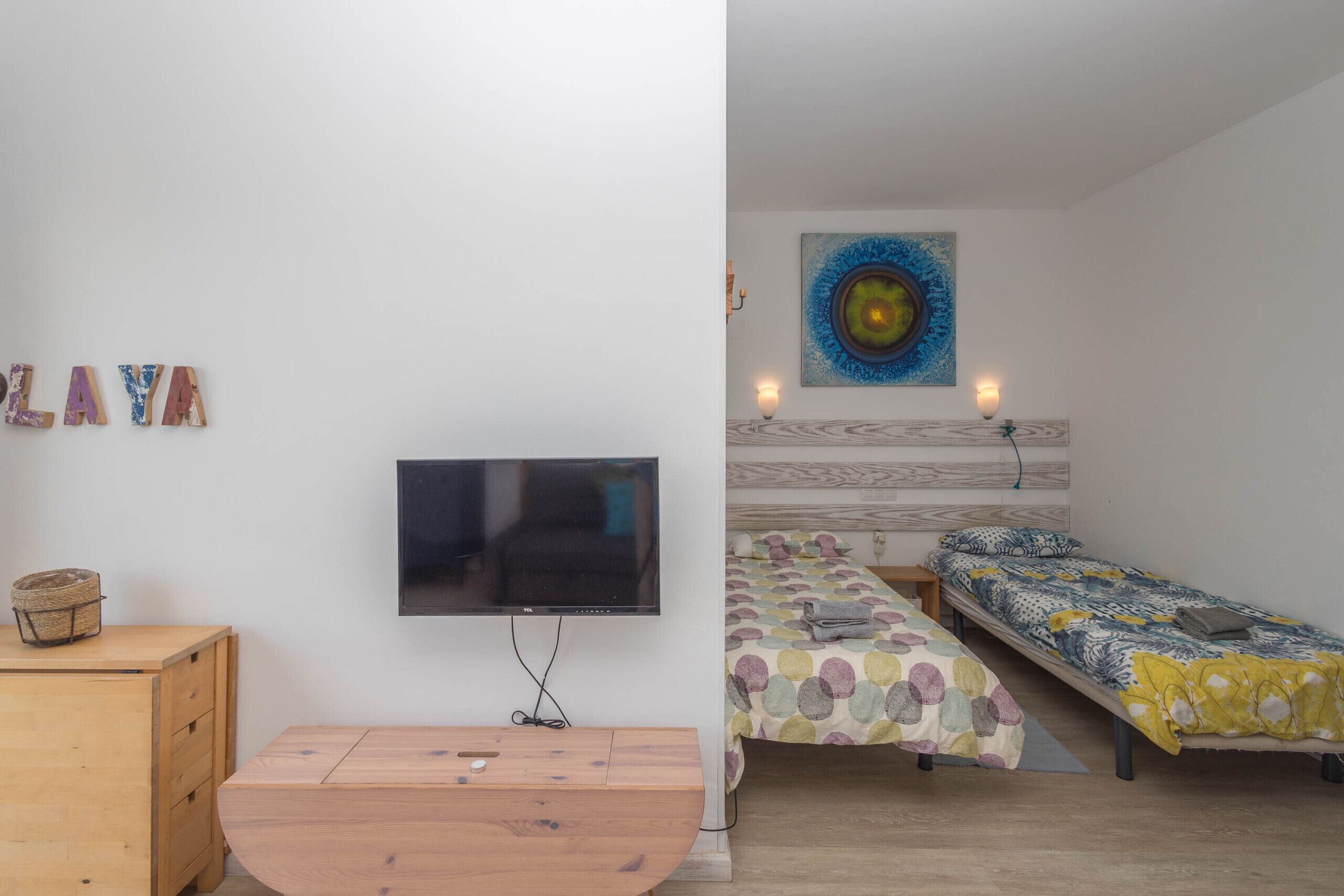 Een slaapkamer met een televisie, twee bedden, een houten dressoir en een kunstwerk aan de muur.