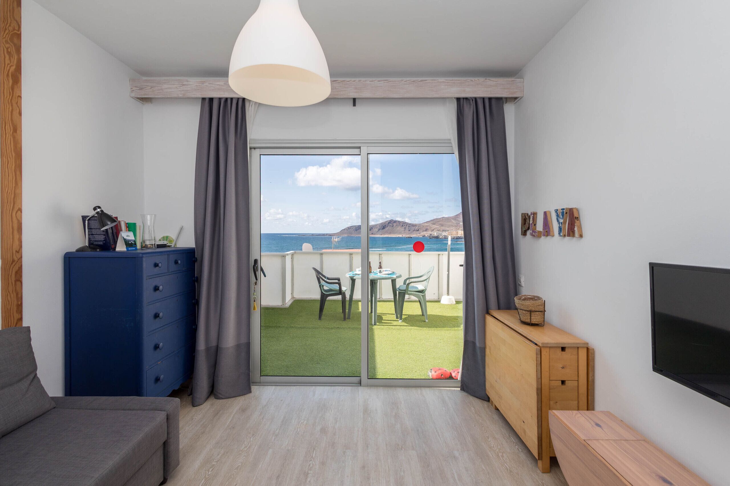 A room with a balcony, a sofa, a TV, and a wooden cabinet.