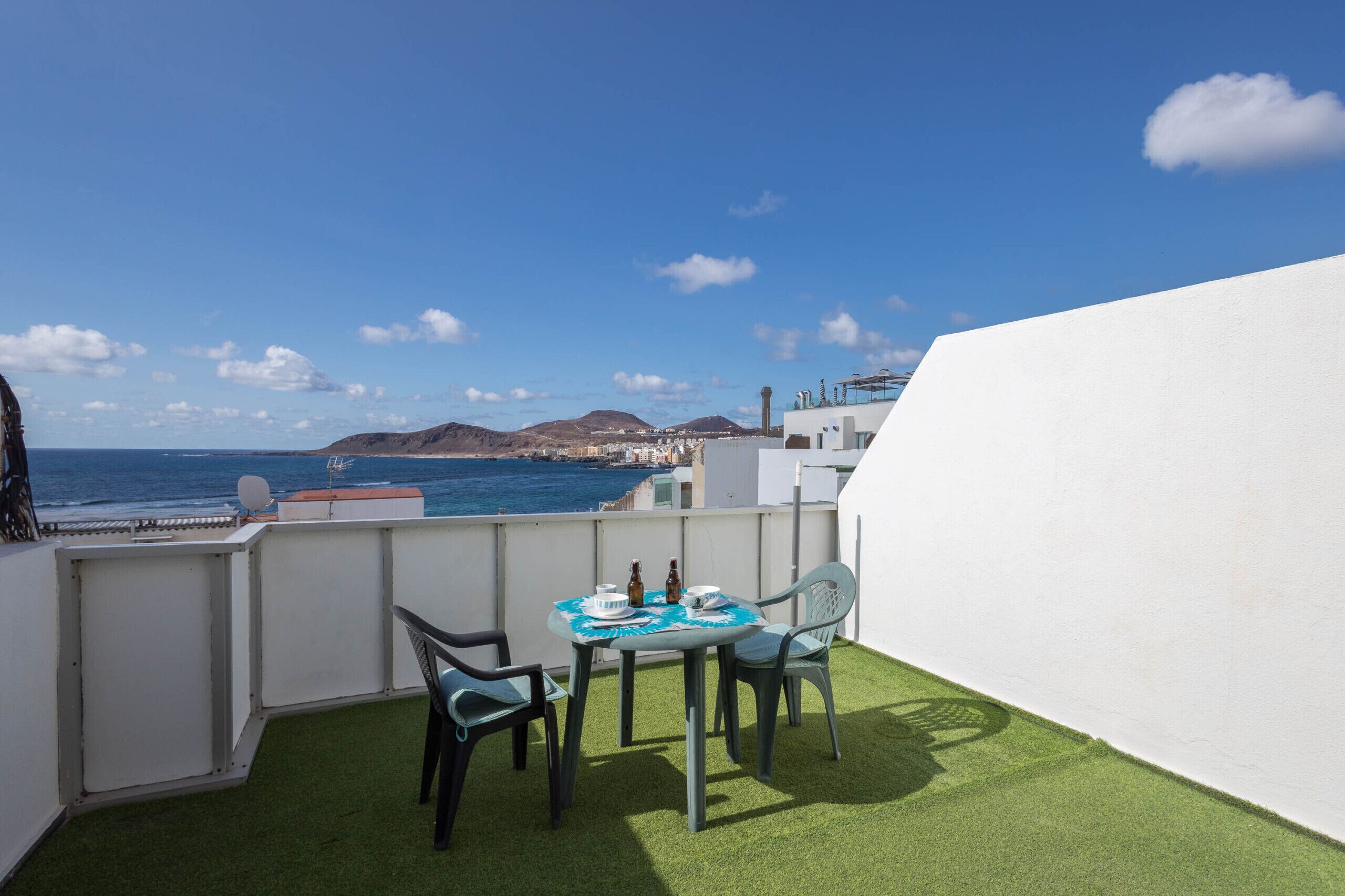A balcony with a table and chairs, a view of the sea, and a white wall.