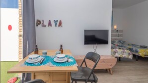 Een kleine kamer met een houten tafel gedekt voor twee personen, een aan de muur bevestigde televisie en een bed met een kleurrijk sprei.