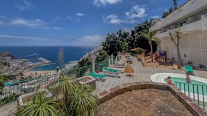 Un resort costero con piscina, vistas al mar y una escalera que lleva a un punto panorámico superior.