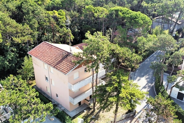 A multi-story building with a red-tiled roof, surrounded by trees, and adjacent to a road.