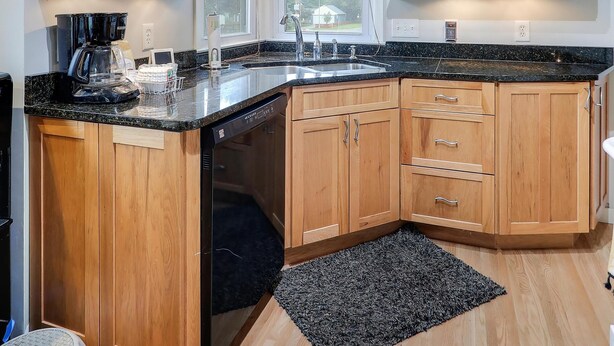 A kitchen with wooden cabinets, a black countertop, and a built-in dishwasher. - The Calm & Comfy Nest (Minneapolis)