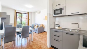 Una cocina moderna con microondas, pileta y muebles grises. Hay un comedor con mesa y sillas, y un sofá al fondo.