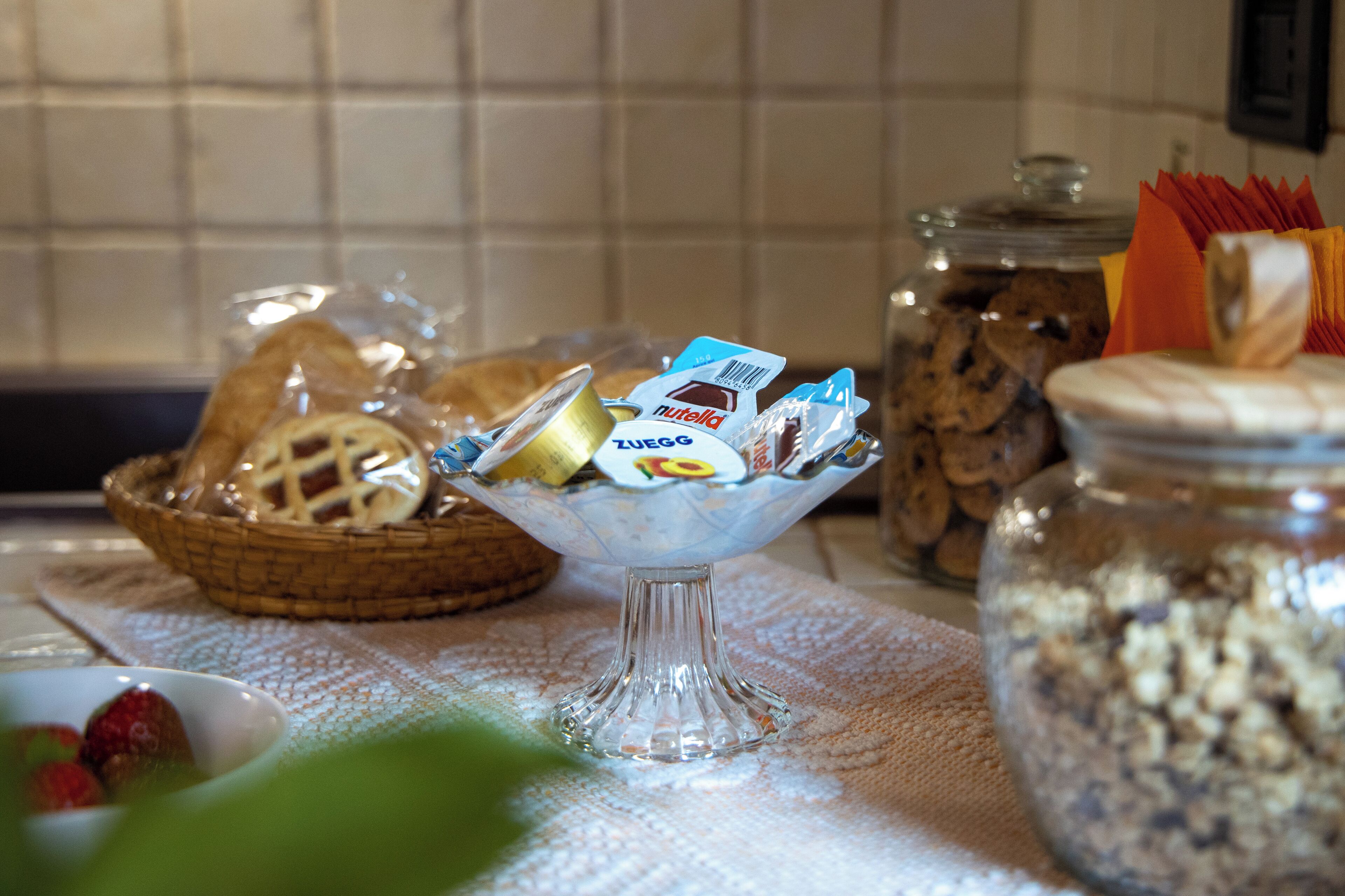 Um buffet de café da manhã com diversas opções de comida, incluindo pães, doces e uma tigela de vidro com Nutella e outras geleias.