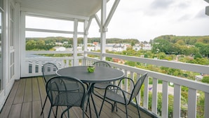 Un espacio al aire libre techado con una mesa y sillas, con vistas a una zona residencial con casas y árboles.