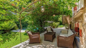 An outdoor patio with wicker furniture, a pergola with hanging lanterns, and lush greenery.
